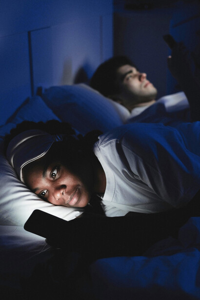 A couple lying in the dark, each absorbed in their smartphone