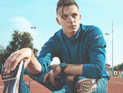 A male runner is seen doing leg stretches as part of his warm-up regimen, gearing up for a focused training session on the stadium tracks