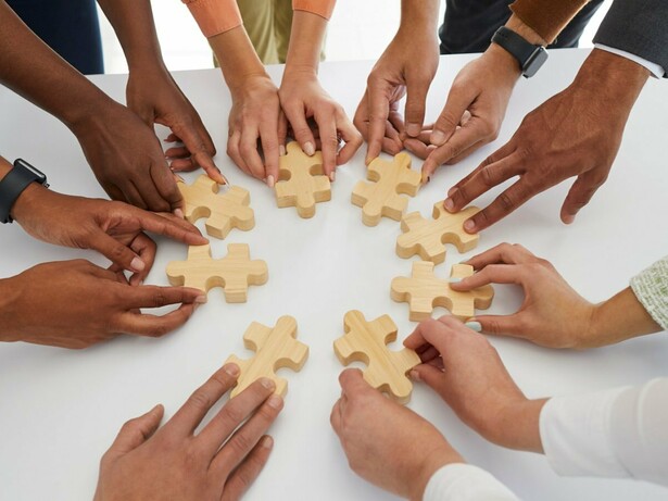 Mãos de diferentes pessoas movimentam peças de um quebra-cabeça sobre uma mesa. A construção coletiva de soluções está no centro da atuação do terceiro setor, que articula pessoas, recursos e competências em torno de objetivos sociais