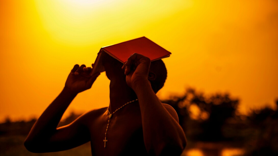 Homem segura um livro aberto diante do rosto, em meio à luz do entardecer. Entre palavras, pensamentos e interpretações, a linguagem também participa da maneira como percebemos e construímos o mundo