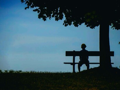 Persona seduta di spalle su una panchina alle prime ore del giorno