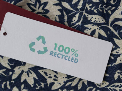 A close-up view of a clothing tag displaying a recycling icon, illustrating the commitment to recycling products