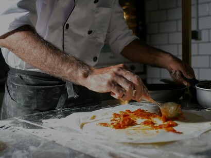 Homem cozinha em feira gastronômica em Portugal. A iniciativa de construir o Centro Interpretativo do Brulhão, conforme destacada pelo presidente da União de Freguesias de Peso e Vales do Rio, visa preservar, mas também promover a cultura e a gastronomia local como um atrativo turístico relevante