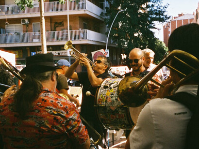 In a Spanish neighborhood at dusk, a group of people plays music on the street, reflecting the resilience and spirit of the community