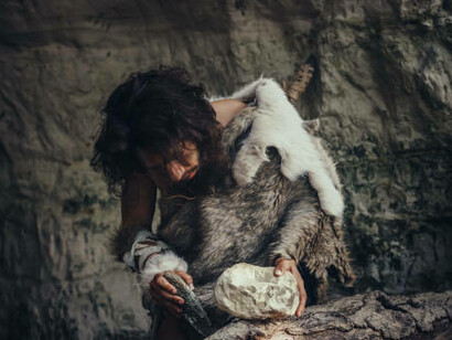 A primeval caveman, dressed in animal skins, holds a sharp stone fitted with a concealed handle—the first primitive tool for hunting. This Neanderthal hand axe marks the dawn of human civilization