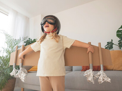 A girl joyfully playing with cardboard wings symbolizes her dreams, imagination, and aspirations for future success
