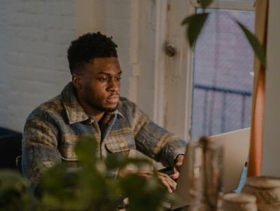 A concentrated Black man works on his laptop and drinks coffee in a café