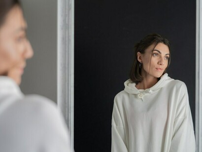 A young woman in a white hoodie standing before a mirror, symbolizing a journey of self-discovery and inner reflection