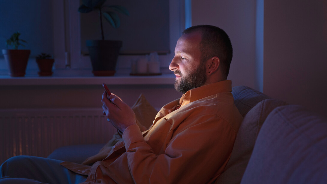 In the dim glow of his phone, a man searches for connection, but the quiet room around him reflects the hollowness of digital intimacy