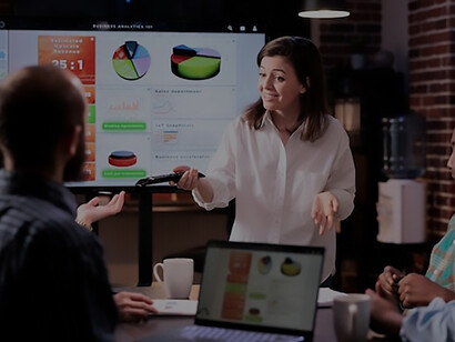 Experience a late-night meeting atmosphere as team members gather around charts on a big TV screen, attentively listening to an employee presenting insightful data on fashion trends and customer preferences, emphasizing the importance of fashion data analysis