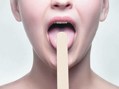 A woman displaying the utilization of a tongue compressor for an ad campaign to raise awareness about the causes of sore throats
