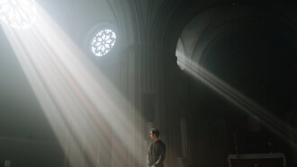 The rays cutting through the darkness serve as a poignant metaphor for the search for truth in a world where faith can be both a refuge and a tool for power 