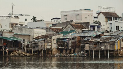L'image présente des habitations traditionnelles sur pilotis en bordure d'un cours d'eau, typiques des paysages fluviaux du delta du Mékong au Vietnam