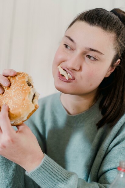 A woman sitting at a table with fried chicken and a hamburger, capturing the allure of junk food and fast-food culture