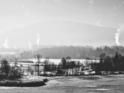 Snow-covered fields stretch toward an industrial horizon, contrasting quiet purity with signs of human impact