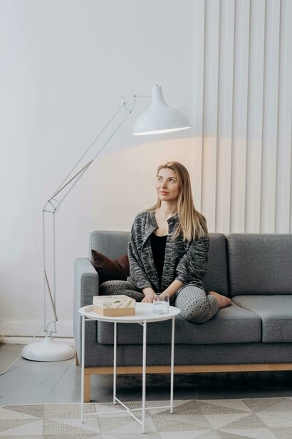 A woman in a black-and-white long-sleeve dress seated on a grey couch at home