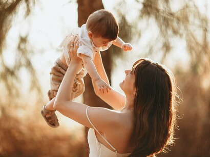 A mother joyfully lifting her baby into the sunlight, representing the secure attachment that lays the foundation for lifelong emotional well-being