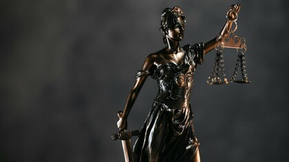 A sculpted defender of law with suspended scales, representing the fragile balance of democratic institutions
