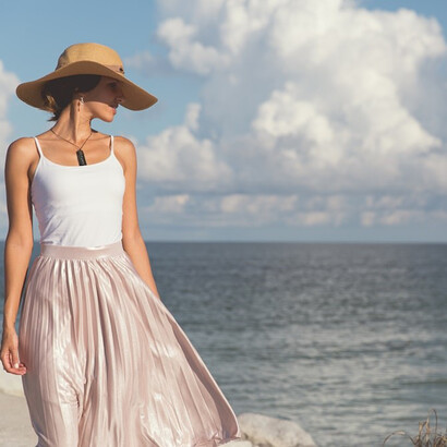 A serene woman stands on the beach, wearing a white skirt, connecting effortlessly with the coastal surroundings