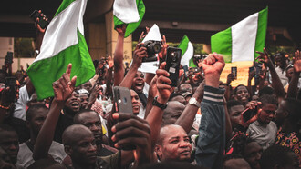 In the heart of Nigeria, amidst waving flags, individuals gather with their phones, showcasing how mobile technology has revolutionized communication, connecting loved ones effortlessly and bridging geographical barriers