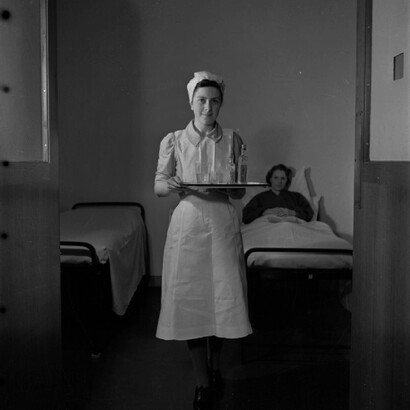 Retrato de una estudiante de enfermería mientras lleva una bandeja desde la cama de un paciente en el Hospital St. Helier. 1943