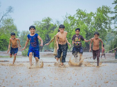 Um grupo de menino atravessas a água de uma rua alagada durante a chuva. Na infância evocada pelo texto, situações que poderiam parecer desconfortáveis tornam-se experiências de liberdade, descoberta e alegria