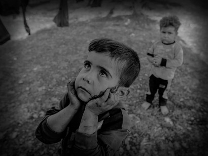 A young boy and his friend playing but looks up with sad eyes, in the Idlib refugee camp, Idlib Governorate, Syria
