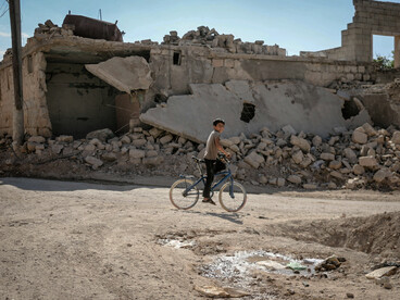 A young boy with his bicycle moves through the wreckage of a destroyed neighbourhood in Idlib, Idlib Governorate, Syria