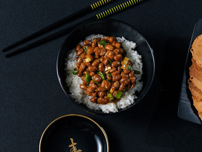 Nattō, a traditional Japanese breakfast dish, consists of whole soybeans fermented using Bacillus subtilis var. natto. It is usually enjoyed with rice and flavored with karashi mustard, soy or tare sauce, and sometimes garnished with Japanese bunching onions
