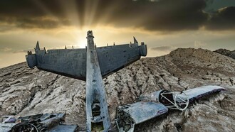 Les débris d'un avion factice se dressent sur un sol rocheux sous un ciel d'orage percé de rayons solaires dramatiques