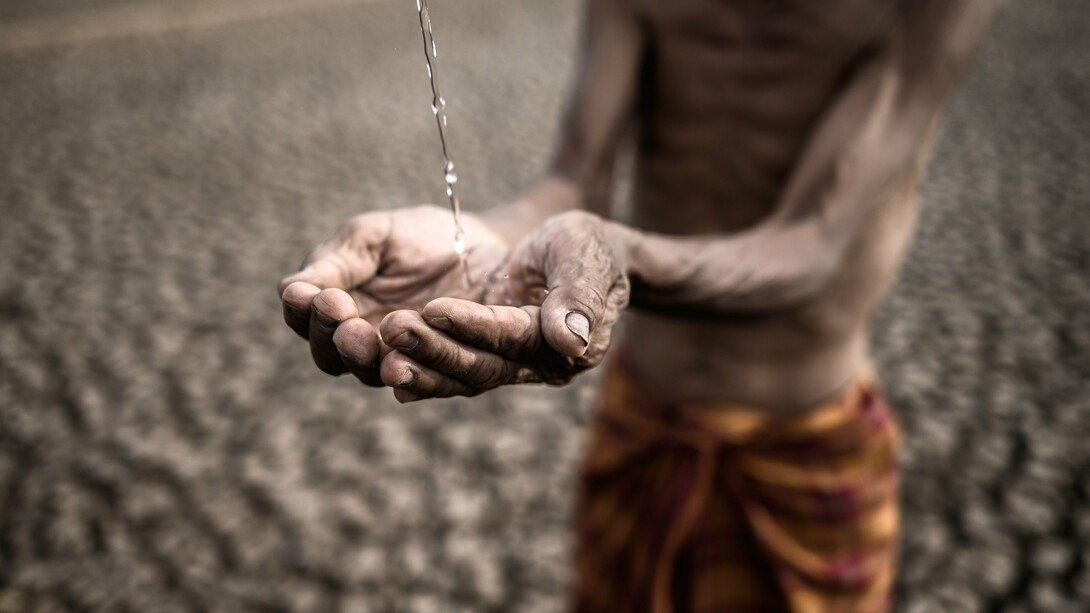 A frail, emaciated man with parched, weathered hands desperately cups a trickle of water against a backdrop of cracked, barren earth—a haunting symbol of extreme drought and deprivation, reflecting the dire consequences of ineffective development aid