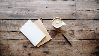 Dos libretas, una tasa de café y un bolígrafo encima de una mesa de madera