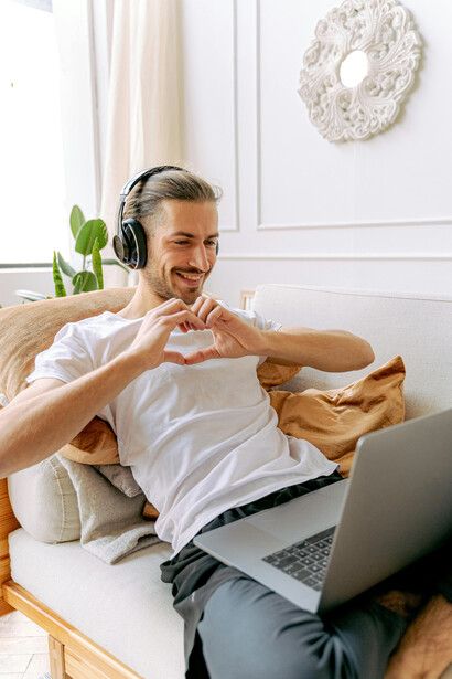 A man talking online makes a heart sign with his hands, expressing affection in a long-distance relationship
