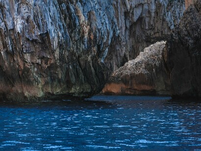 Towering volcanic cliffs enclosing a dark blue sea cave, symbolizing the wild coastline and hidden adventures that is found in Milos
