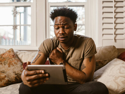 An emotional man sitting on a couch, watching something on his tablet