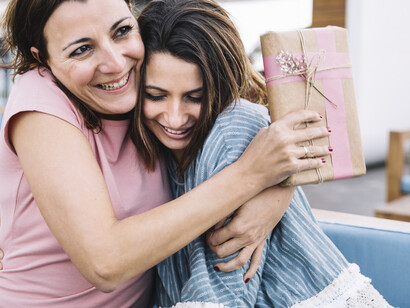 A daughter gives a gift and hugs her mother on the sofa for Mother’s Day
