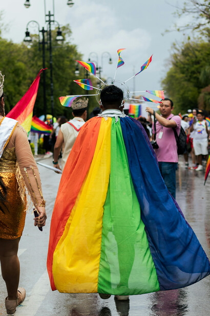 A person wearing a cape and halo crown, adorned with LGBT flags, at a pride parade