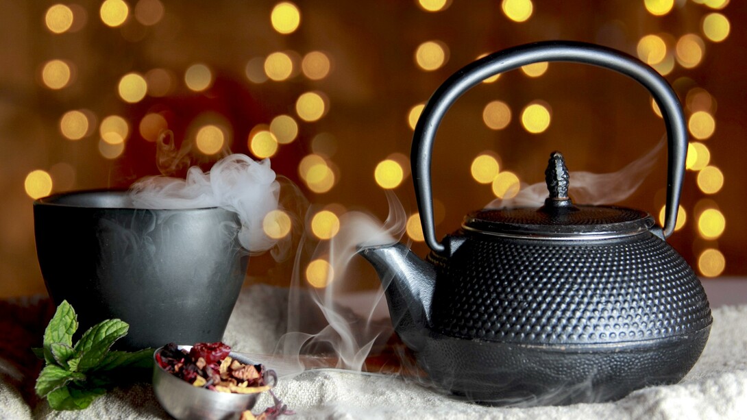 Chaleira e xícara exalam vapor de chá de menta com infusão de morangos