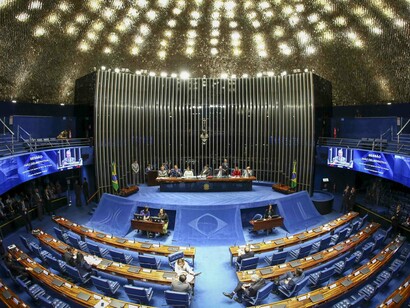 Parlamentares ocupam o Plenário do Senado Federal durante uma sessão, enquanto os painéis eletrônicos exibem informações dos trabalhos legislativos. A dinâmica parlamentar integra o processo de definição das prioridades que orientam a destinação dos recursos públicos