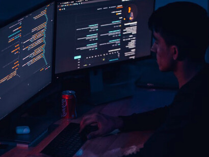 A man in a black long-sleeve shirt sits at his computer