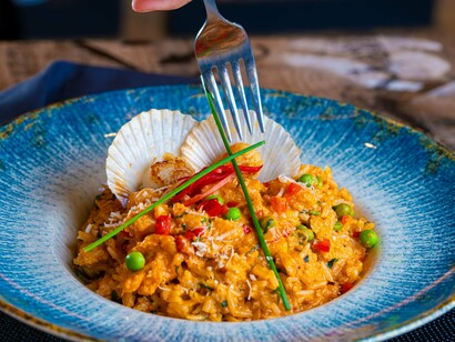 Um prato de paella é servido em uma tigela de cerâmica, destacando ingredientes coloridos e apresentação cuidadosa. A beleza da comida também faz parte da experiência de quem cozinha para encantar