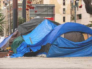 Rows of homeless encampments standing in stark contrast to the luxury apartment buildings towering behind them