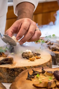 A culinary maestro meticulously assembles a vibrant vegetable dish, arranging the colorful medley with precision on a rustic tree slab, transforming the act of preparation into an artful display of culinary craftsmanship