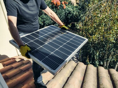 A rooftop worker in a black shirt carefully positions a solar panel for installation