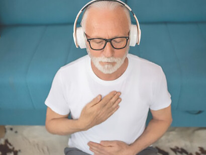 In the quiet sanctuary of his home, a seasoned senior gentleman finds solace as he sits on the floor, immersed in a session of guided meditation, embracing the profound concept of relaxing both his body and mind