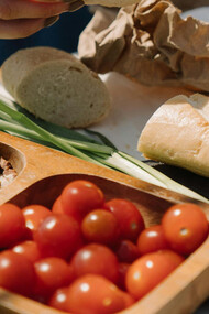 An assortment of healthy food on a table, including: cherry tomatoes, nuts, leaks and sliced bread