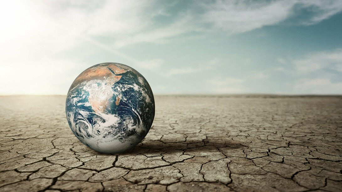 A lone Earth sits on parched, cracked land under a hazy sky, starkly illustrating the devastating impact of global climate change