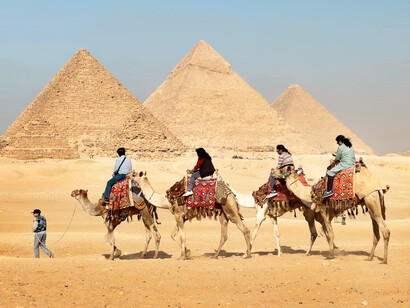 A group of four riders on camels, with the majestic Giza Pyramids in the background, Egypt