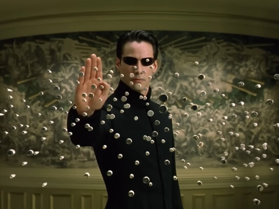 Neo suspending hundreds of bullets in midair with a raised hand, representing one of The Matrix Reloaded's defining moments as he surpasses the limits of the simulated world