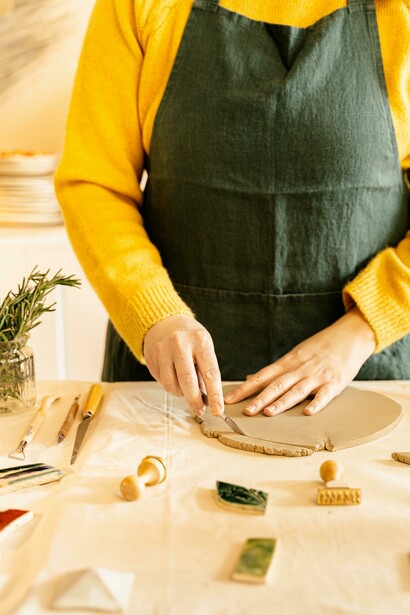 A person wearing an apron molds clay on a worktable during an art activity